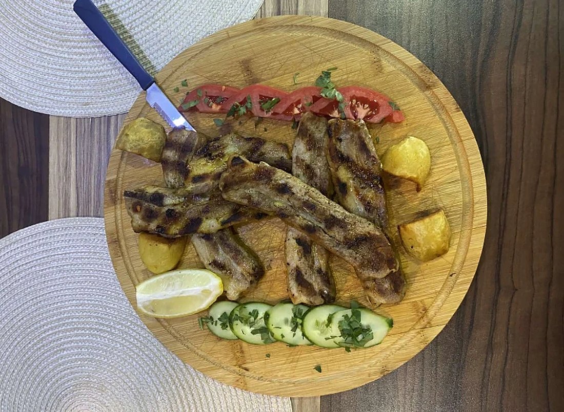 Месо на скара върху дървена дъска, с печени картофи, домати и краставици